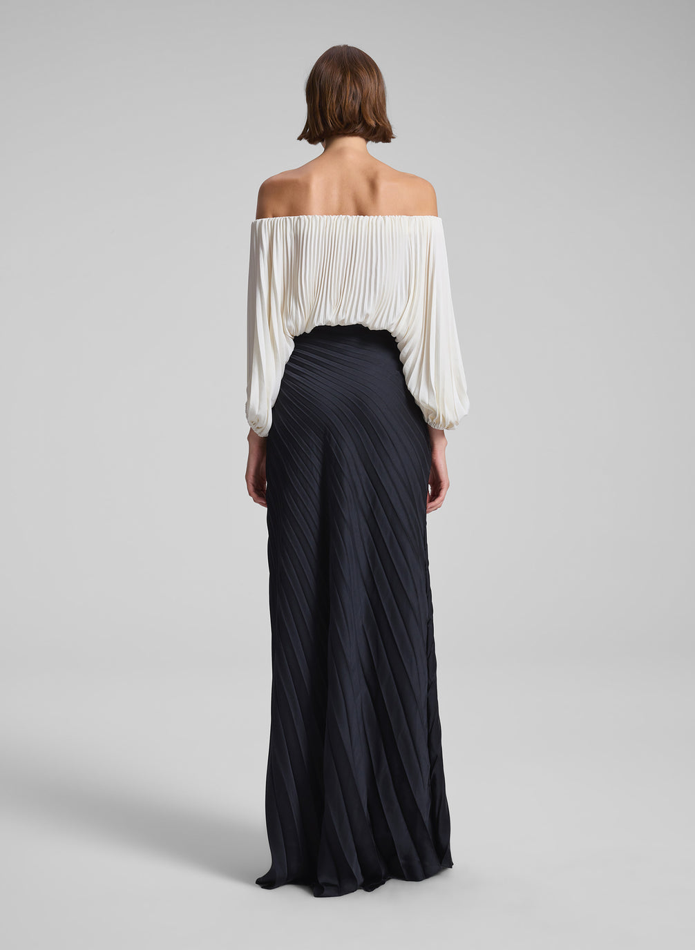 woman wearing white pleated top and black pleated maxi skirt