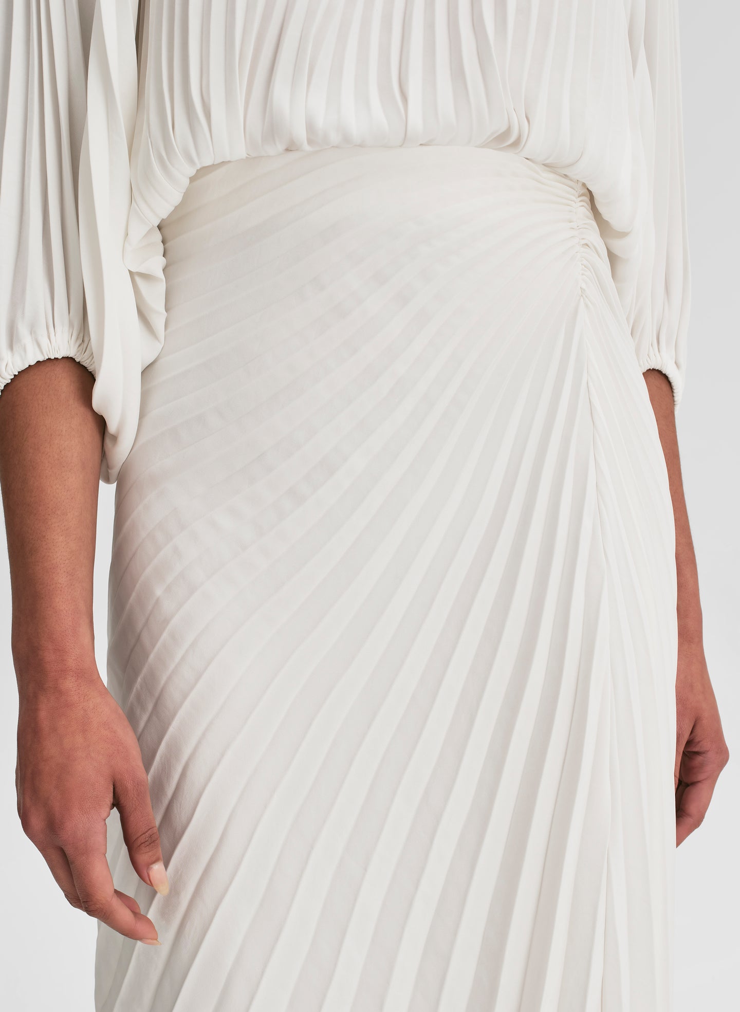 woman wearing pleated off shoulder top and pleated maxi skirt in white