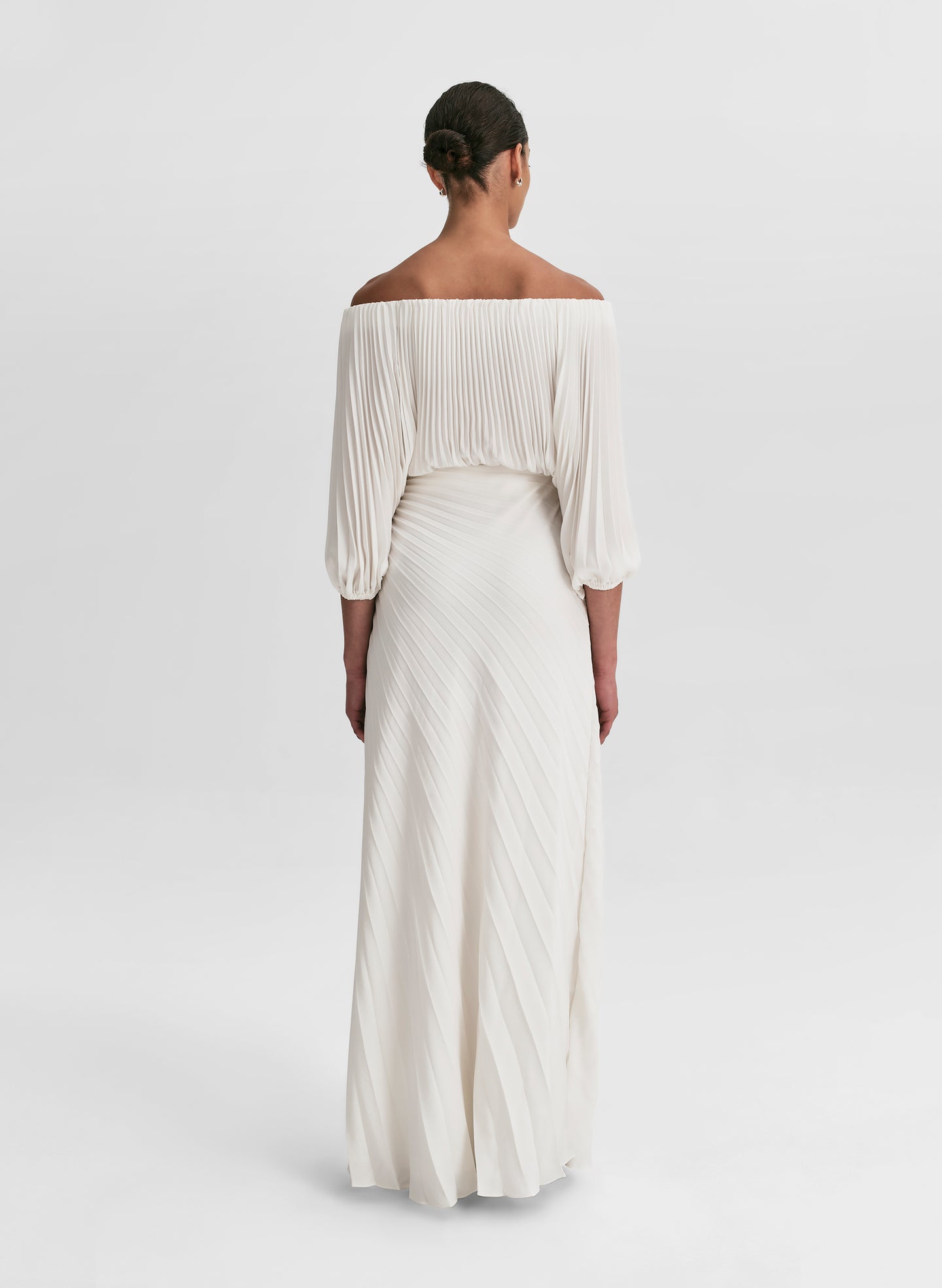 woman wearing pleated off shoulder top and pleated maxi skirt in white