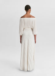 woman wearing pleated off shoulder top and pleated maxi skirt in white
