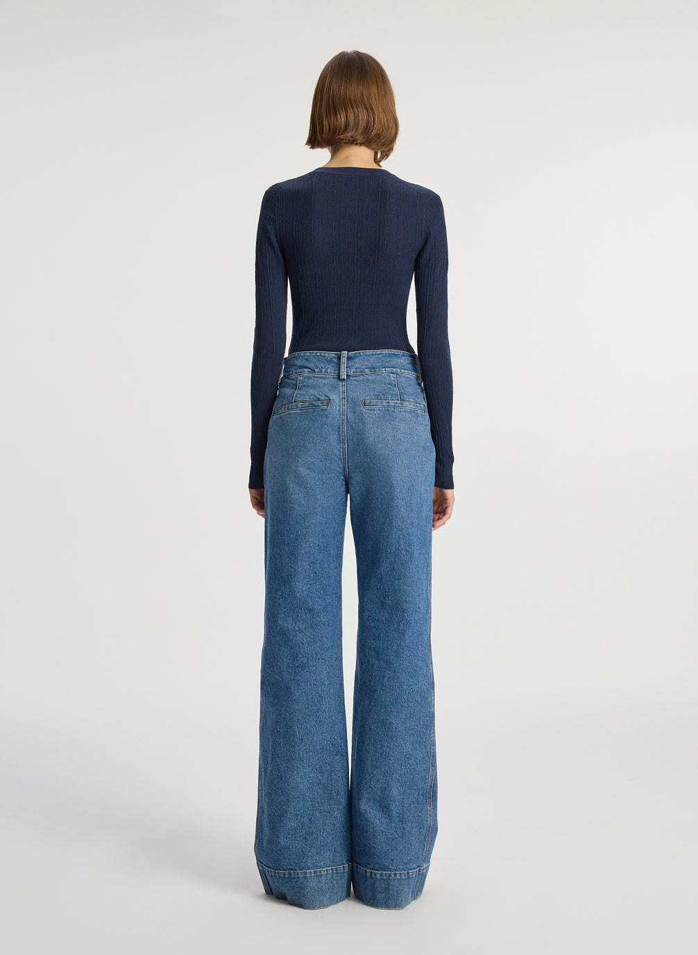 back view of woman wearing navy blue cardigan and medium blue wash wide leg denim jeans
