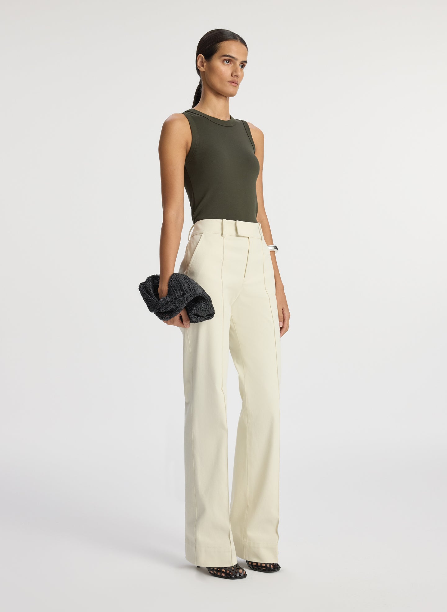 side view of woman wearing olive green sleeveless top with cream wide leg pants