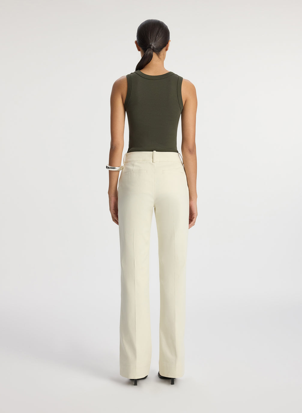 back view of woman wearing olive green sleeveless top with cream wide leg pants
