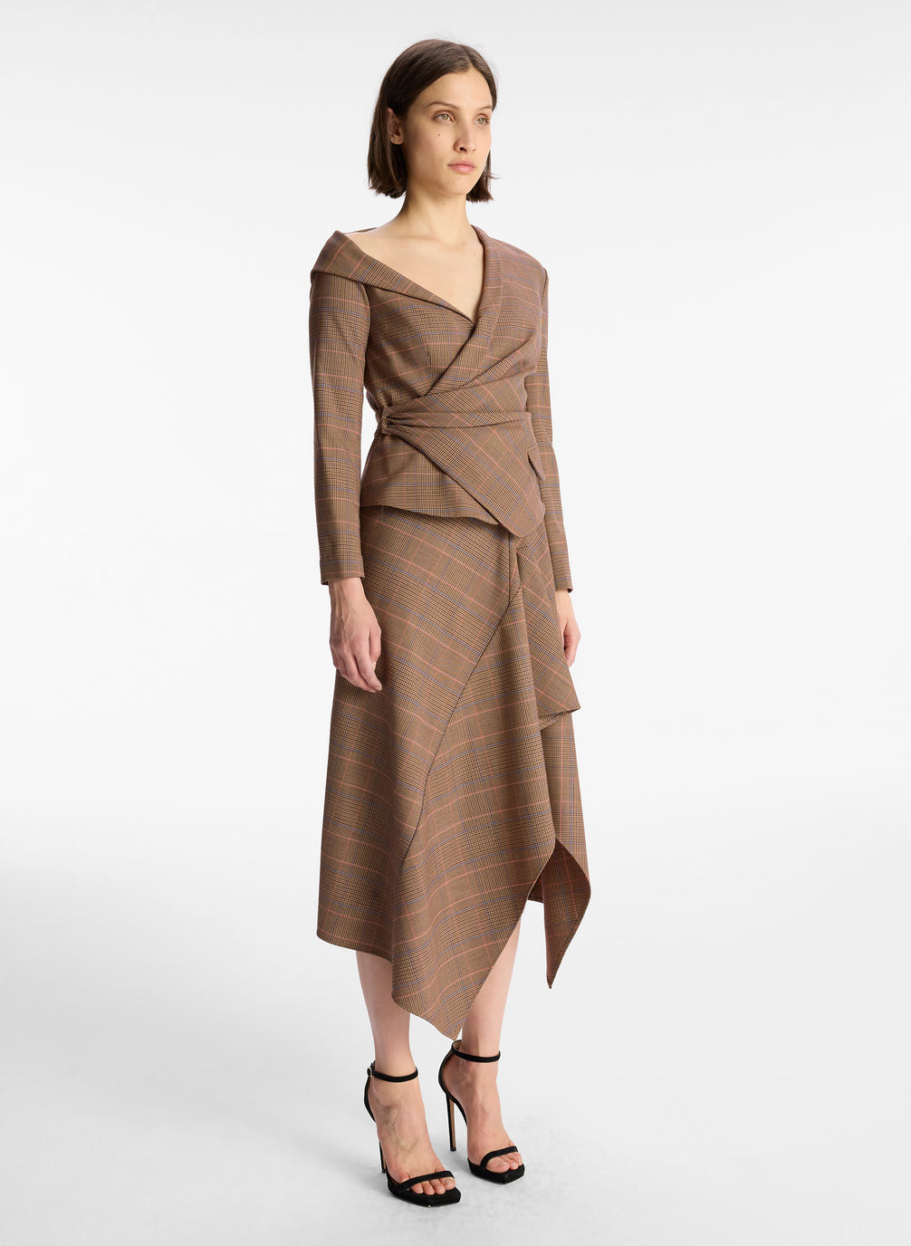 side view of woman wearing brown plaid asymmetric long sleeve top and matching brown plaid midi skirt