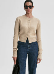 Woman wearing a beige cardigan and blue jeans on a light gray background