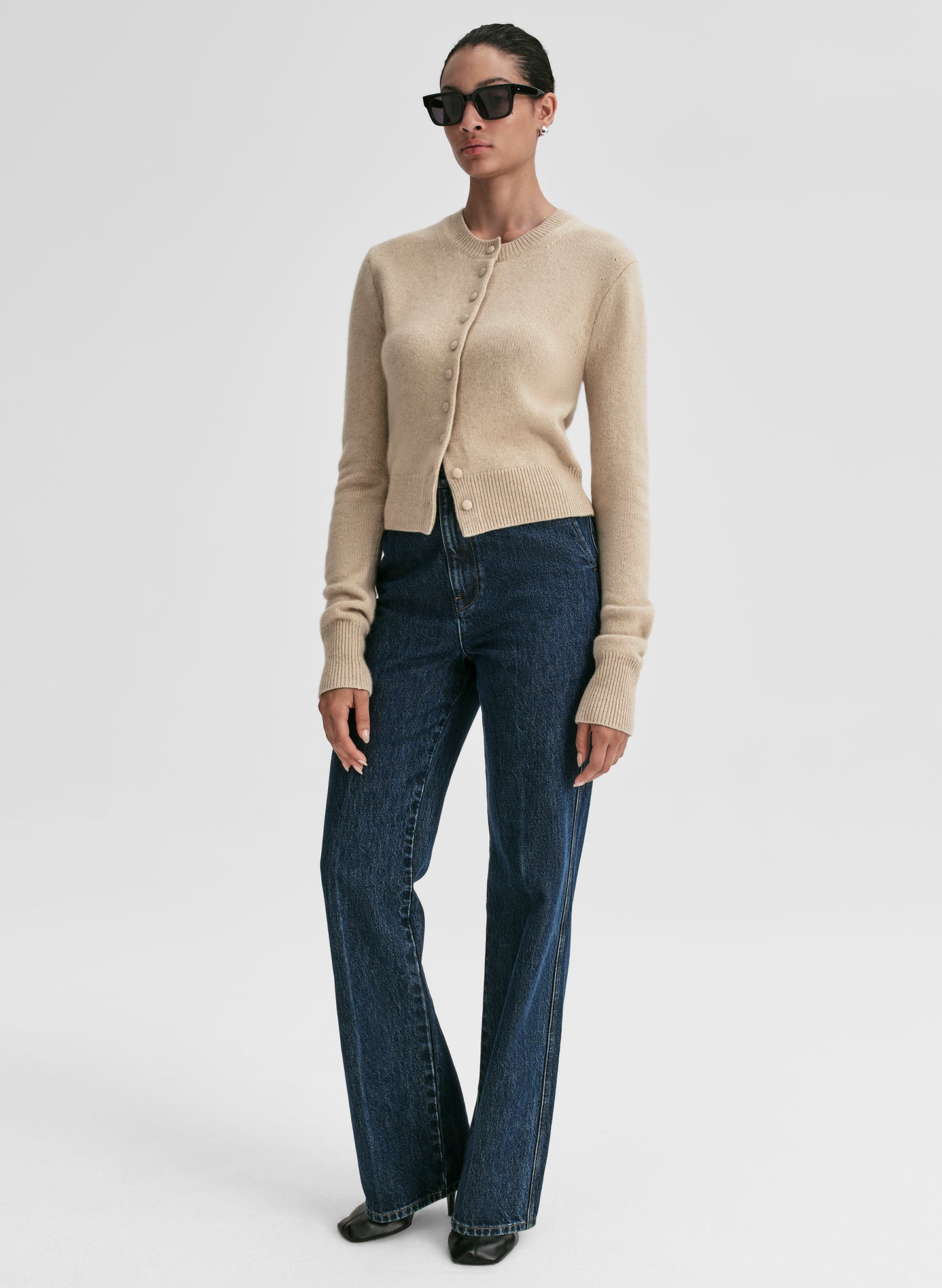 Woman wearing a beige cardigan and blue jeans on a white background