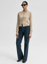 Woman wearing a beige cardigan and blue jeans on a white background