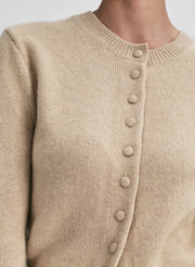 Close-up of a beige cardigan with button details on a neutral background