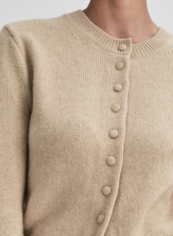 Close-up of a beige cardigan with button details on a neutral background
