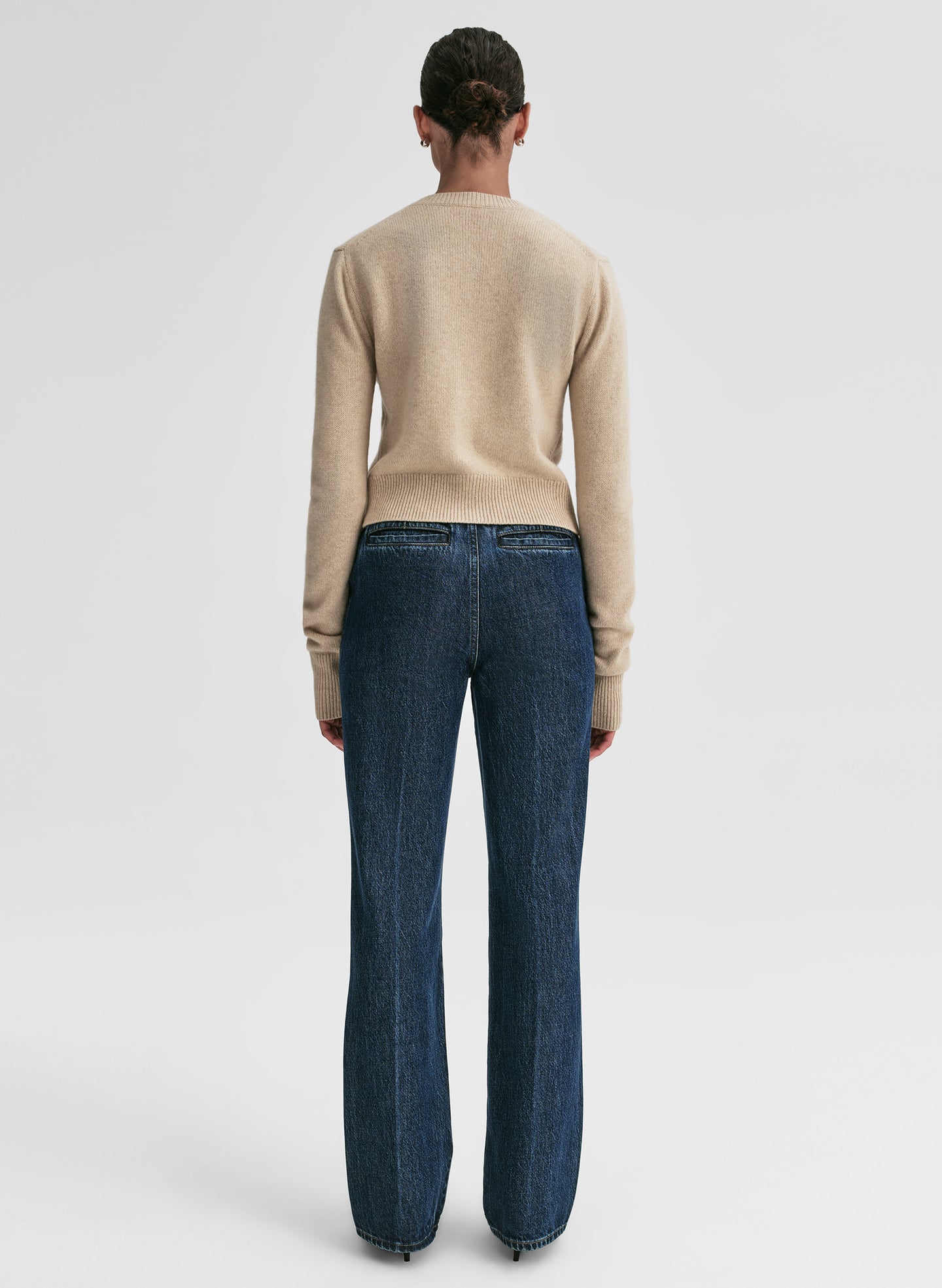 Person wearing a beige sweater and blue jeans on a white background