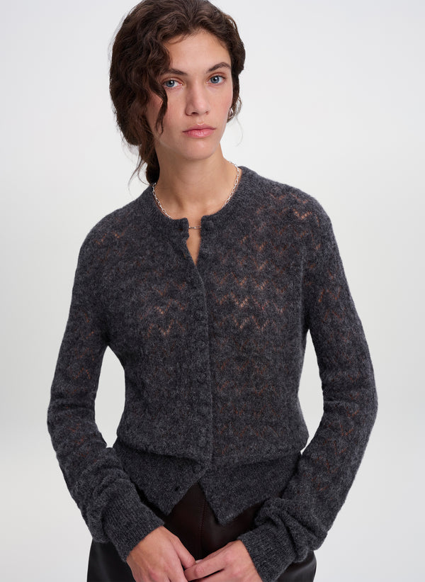A woman wearing a dark charcoal gray textured knit cardigan with a subtle geometric pattern, photographed against a clean light gray studio background.