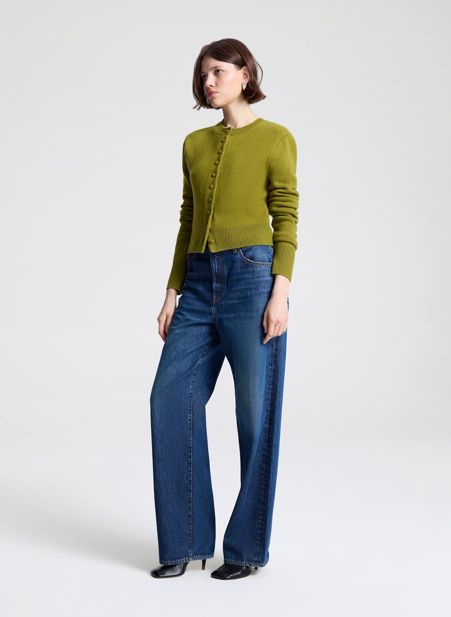 Woman wearing a green cardigan and blue jeans on a white background