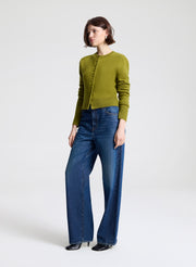 Woman wearing a green cardigan and blue jeans on a white background