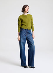 Woman wearing a green cardigan and blue jeans on a white background