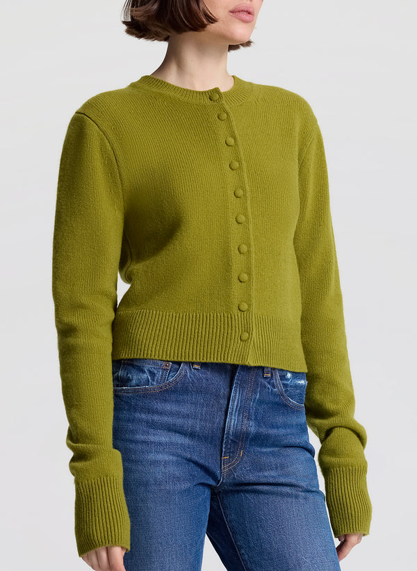 Person wearing a green cardigan and blue jeans on a white background