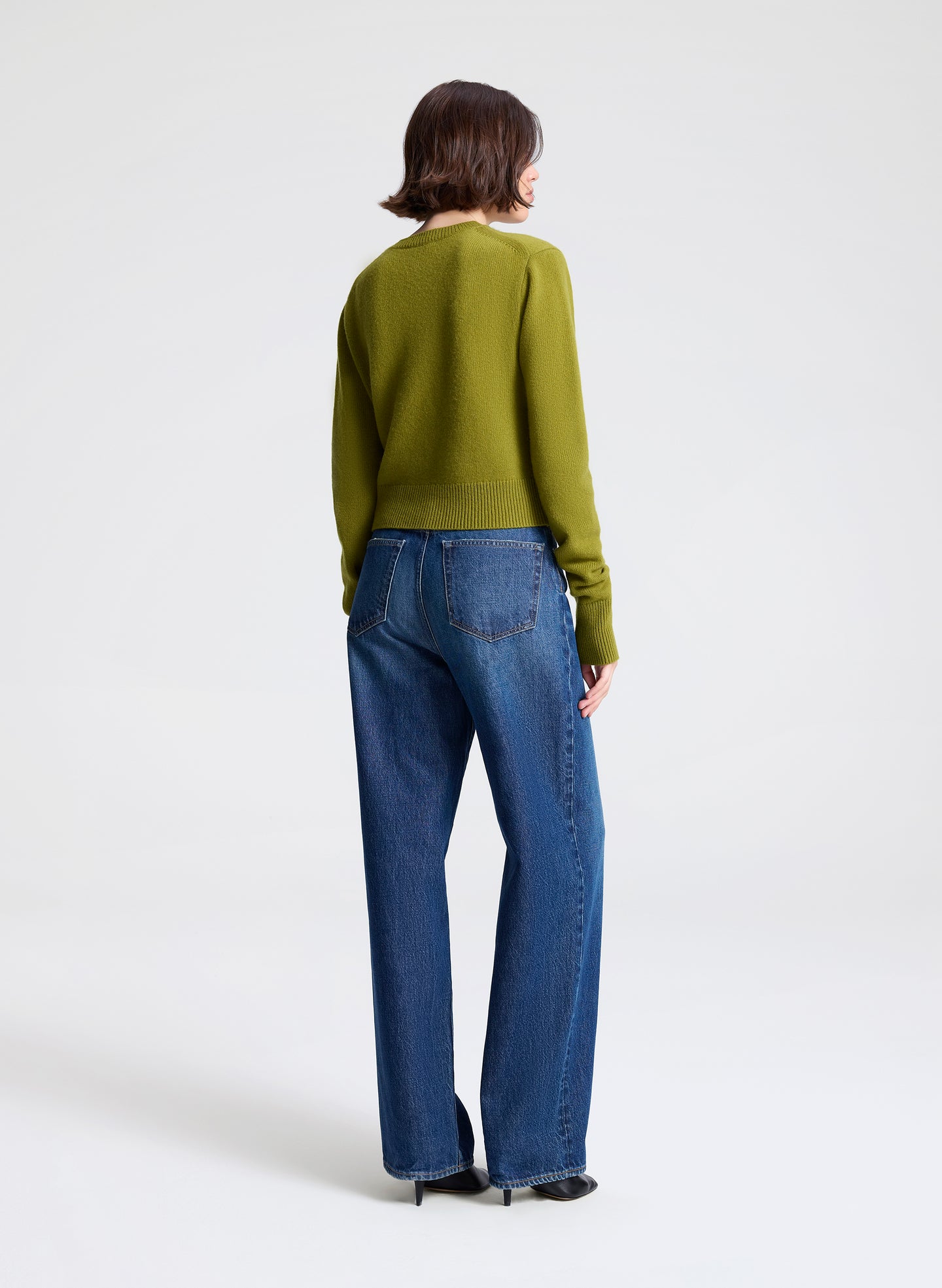 Person wearing a green sweater and blue jeans on a white background