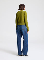 Person wearing a green sweater and blue jeans on a white background