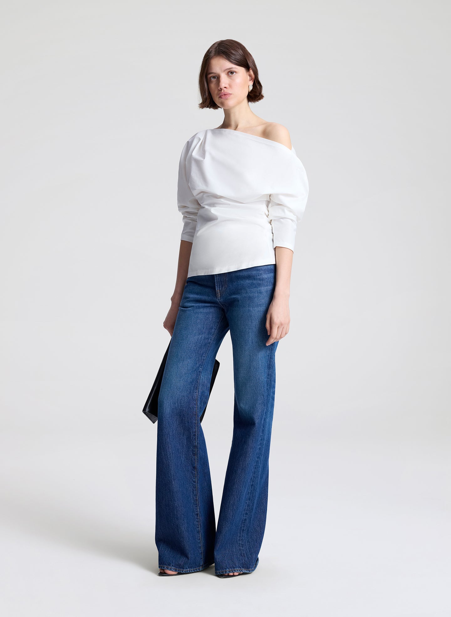 Woman wearing a white off-shoulder top and blue jeans on a light gray background