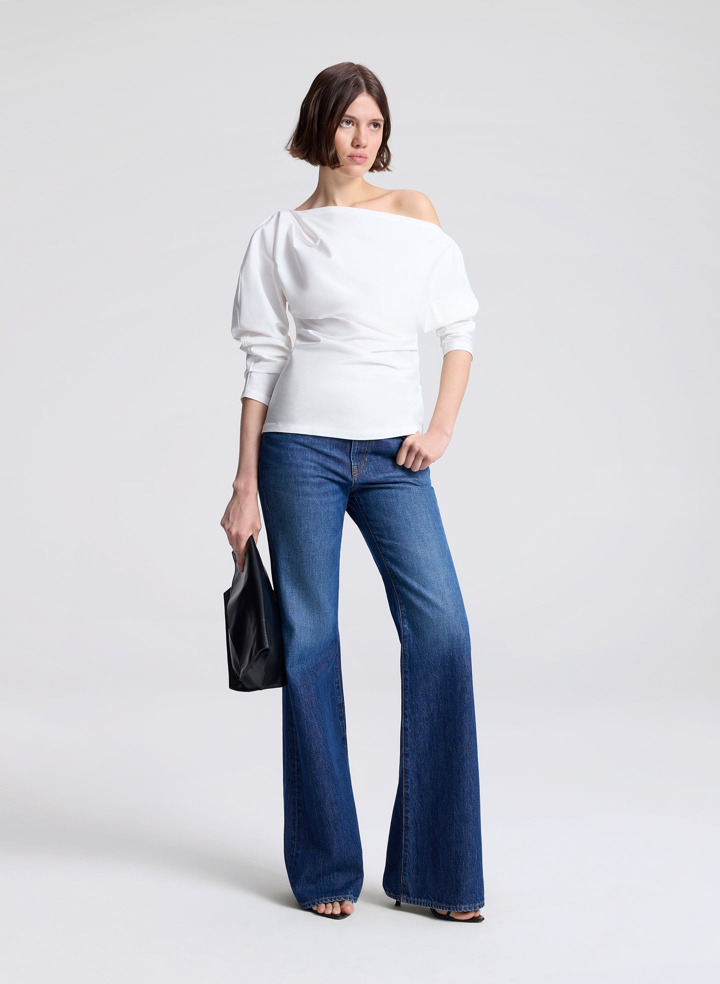 Woman wearing a white off-shoulder top and blue jeans on a light gray background