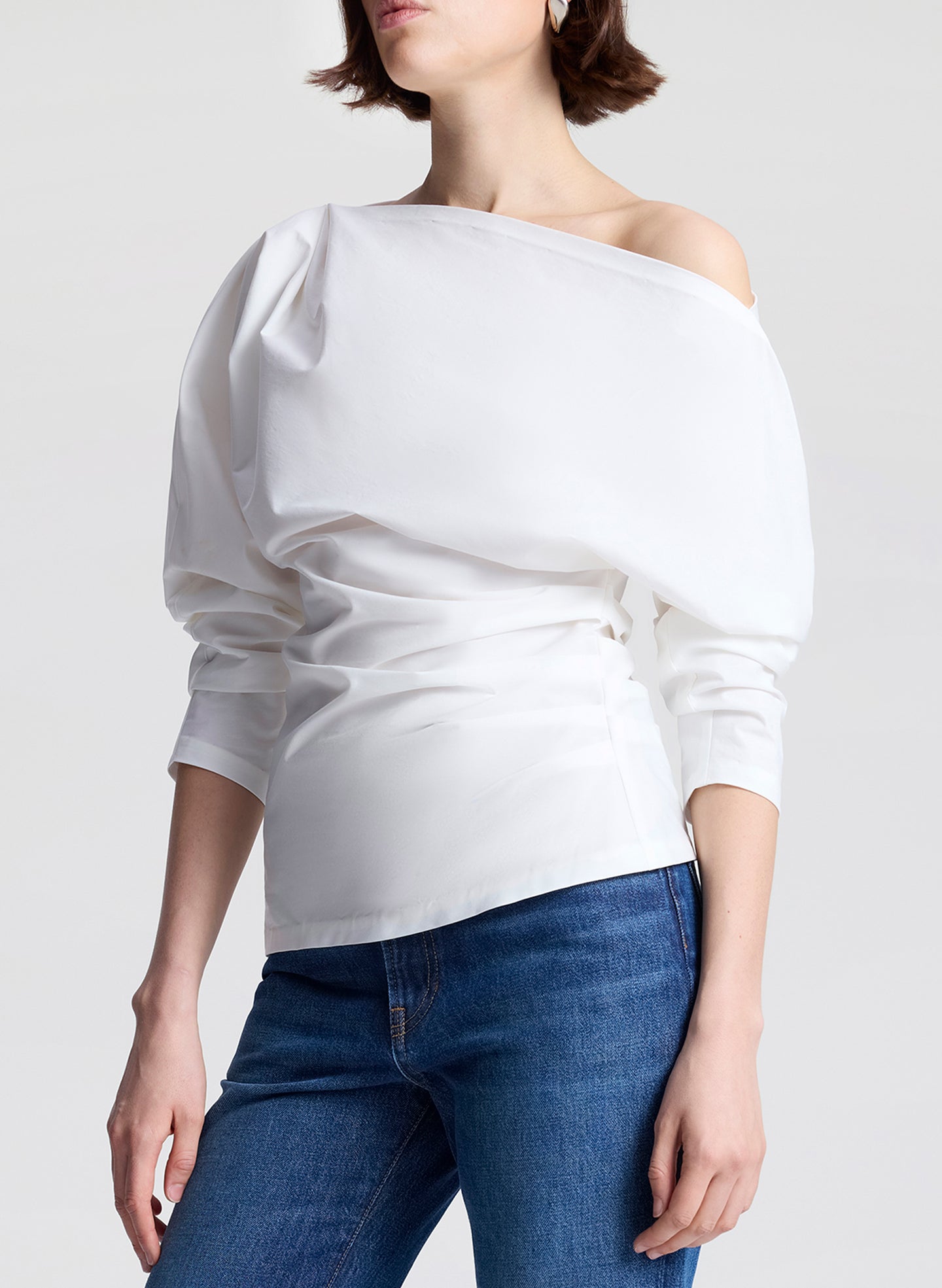 Person wearing a white off-shoulder top and blue jeans on a plain background