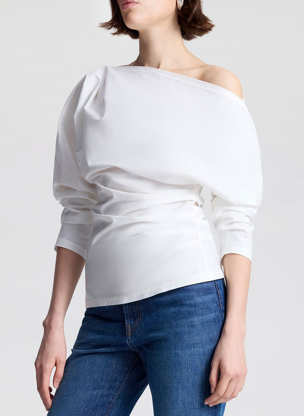 Person wearing a white off-shoulder top and blue jeans on a plain background