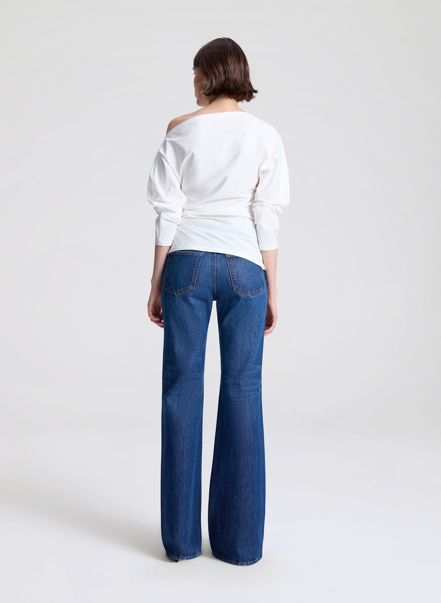 Person wearing a white off-shoulder top and blue jeans on a white background