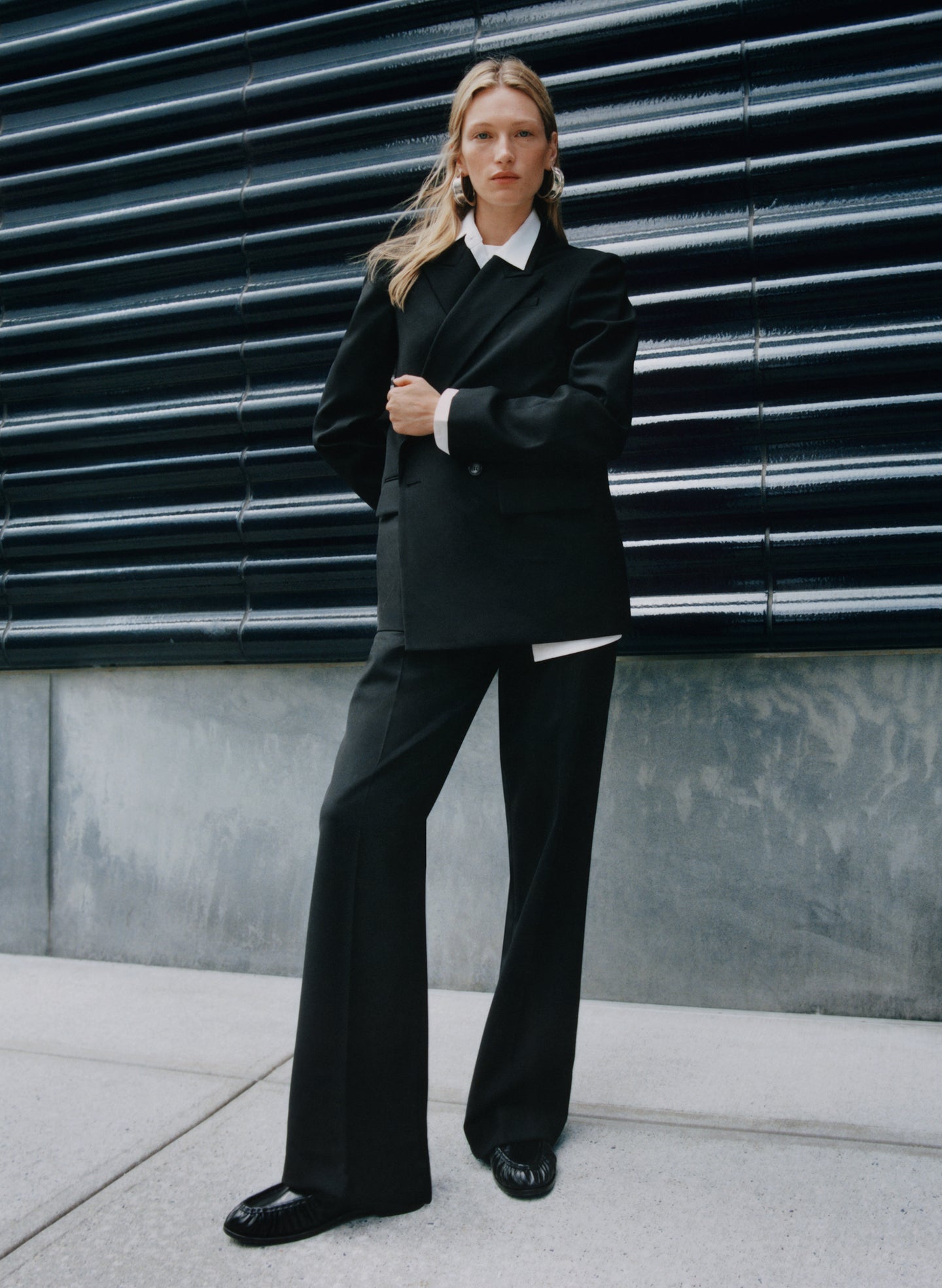 Person wearing a black suit standing against a dark wall.