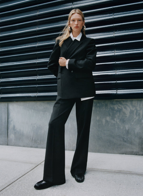 Person wearing a black suit standing against a dark wall.