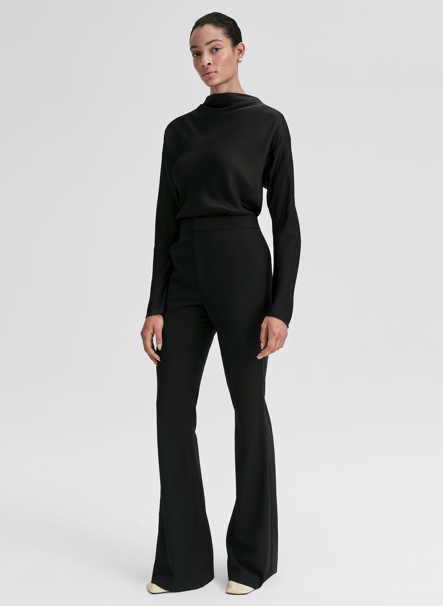 Woman wearing a black outfit with a high neckline and flared pants on a white background