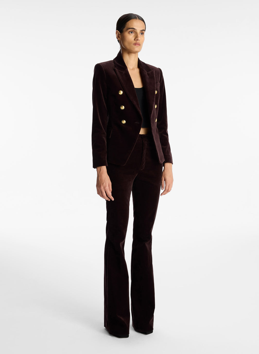 side view of woman wearing brown velvet jacket with gold buttons and brown velvet flared pants