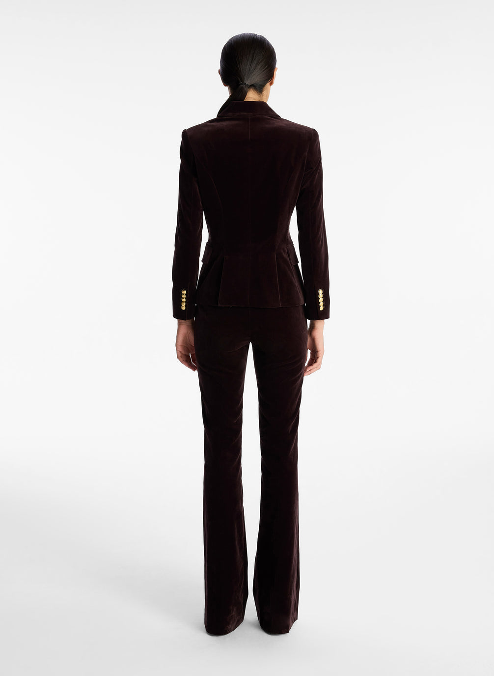 back view of woman wearing brown velvet jacket with gold buttons and brown velvet flared pants