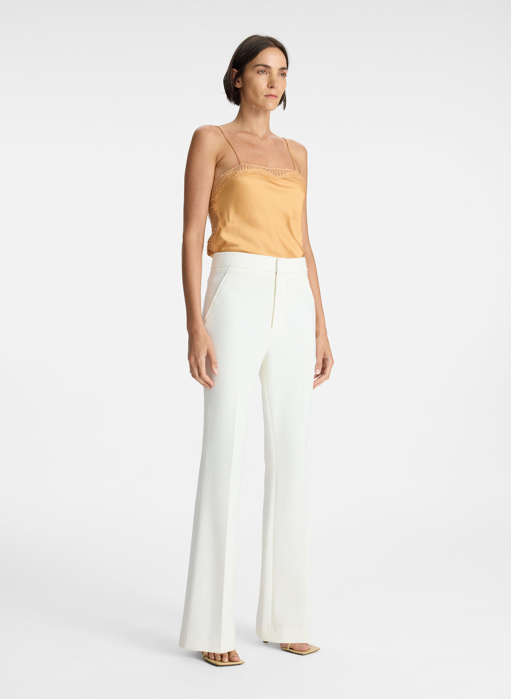 side view of woman wearing beige camisole and white pants
