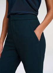 Close-up of a model wearing dark green high-waisted trousers with side pockets and a matching dark green top against a light gray studio background.