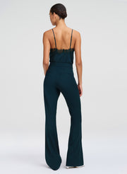 A woman shown from the back wearing a dark teal top with thin straps and a lace-trimmed back and pants, photographed against a light gray studio background.