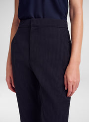 A close-up of a model wearing dark navy blue pinstripe trousers and a matching dark top against a light gray studio background.