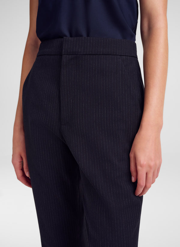 A close-up of a model wearing dark navy blue pinstripe trousers and a matching dark top against a light gray studio background.