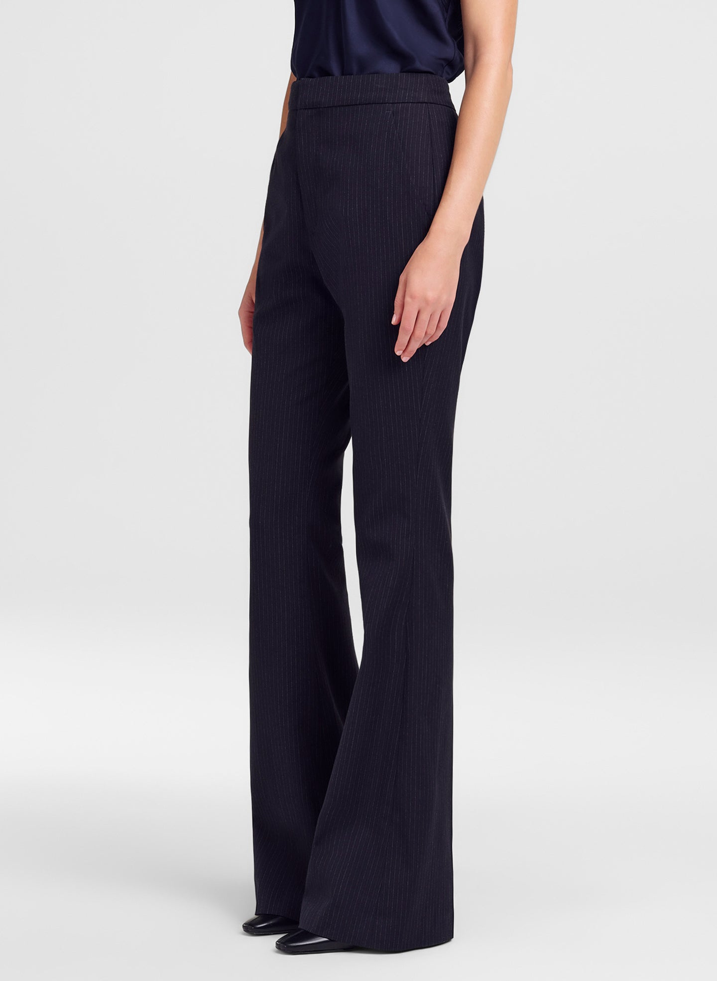 A model wearing high-waisted, wide-leg navy blue pinstripe trousers, shown from the waist down against a light gray studio background.