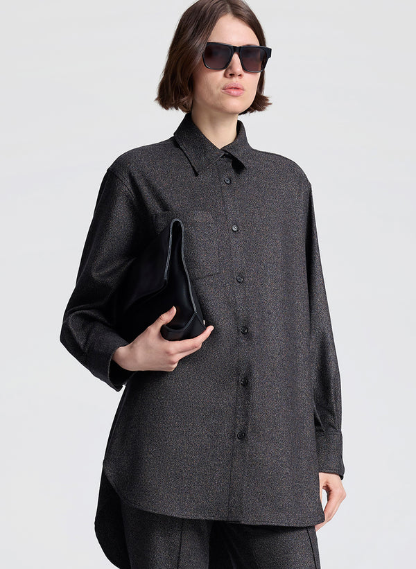 Person wearing a dark gray button-up shirt and sunglasses, holding a black clutch against a light gray background