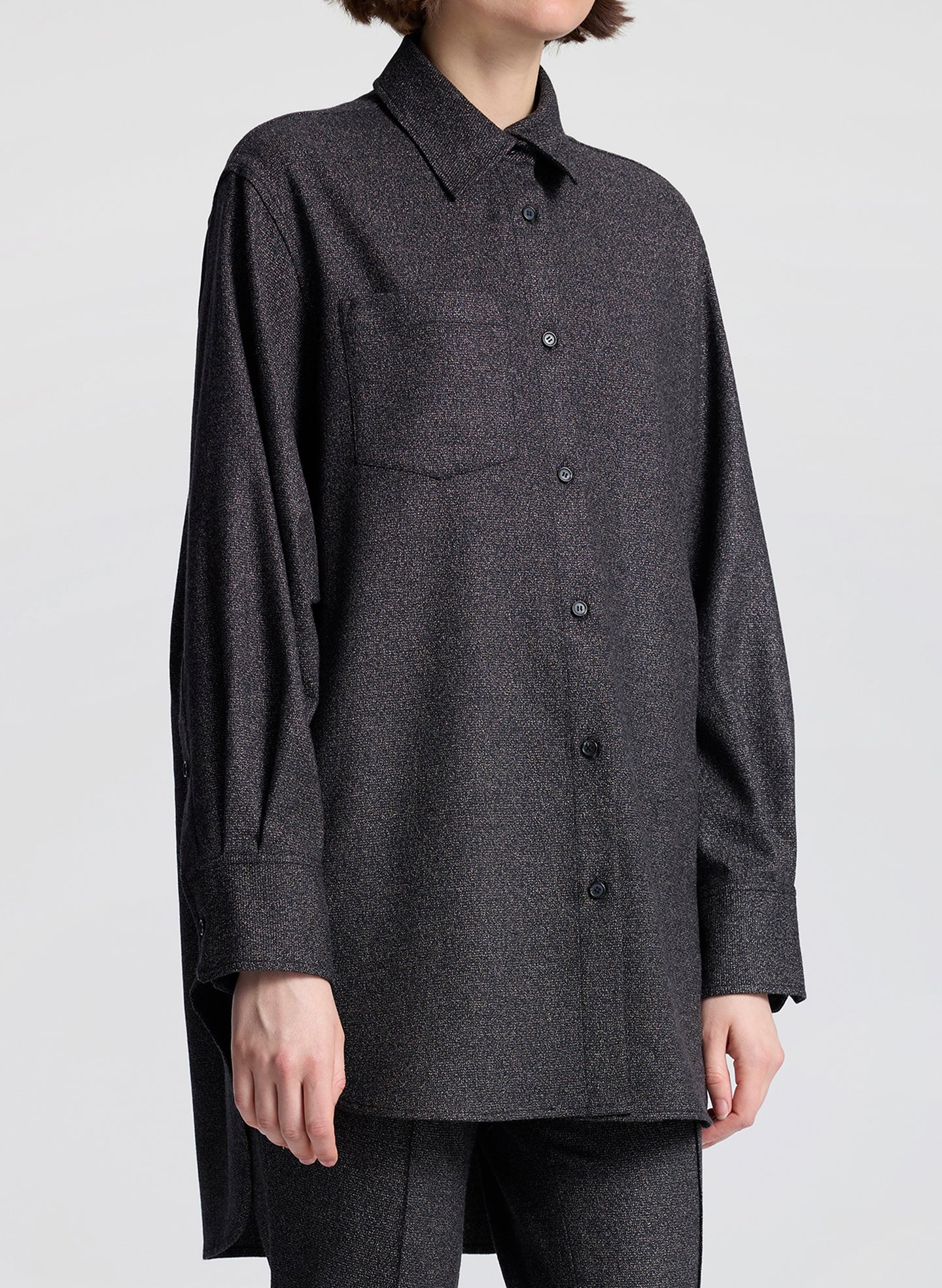 Person wearing a dark gray button-up shirt with a plain background