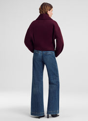 A model shown from the back wearing a dark burgundy cropped jacket and blue wide-leg jeans against a light gray studio background.
