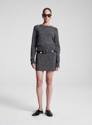 Woman wearing a gray sweater and skirt with a belt on a white background