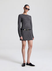 Person wearing a dark gray speckled sweater and skirt with a black belt on a white background