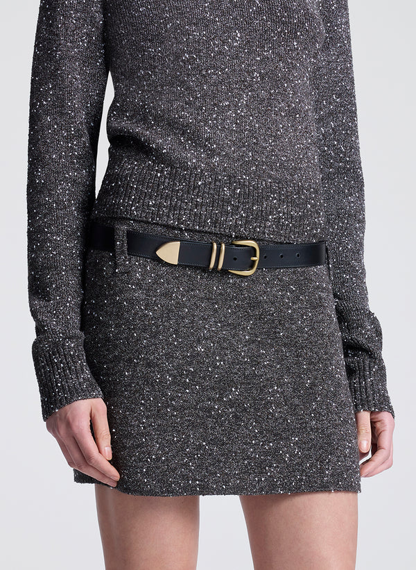 Person wearing a dark gray speckled sweater and skirt with a black belt on a white background