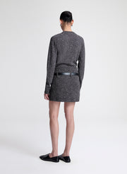 Person wearing a dark gray speckled sweater and skirt with a black belt on a white background