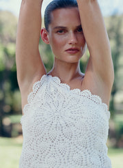 Woman wearing a white crochet top with a blurred natural background