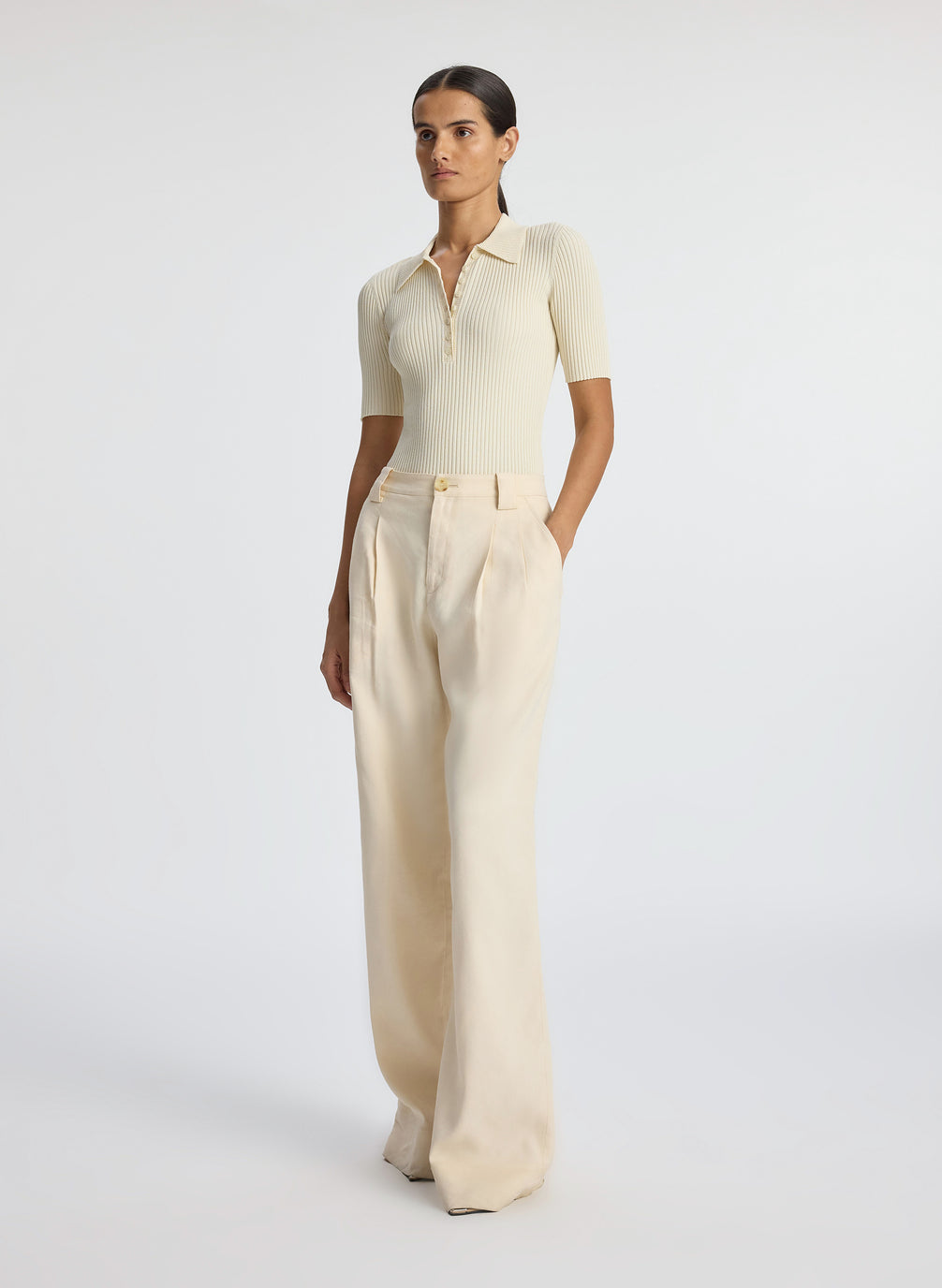 side view of woman wearing cream short sleeve collared top and beige pants
