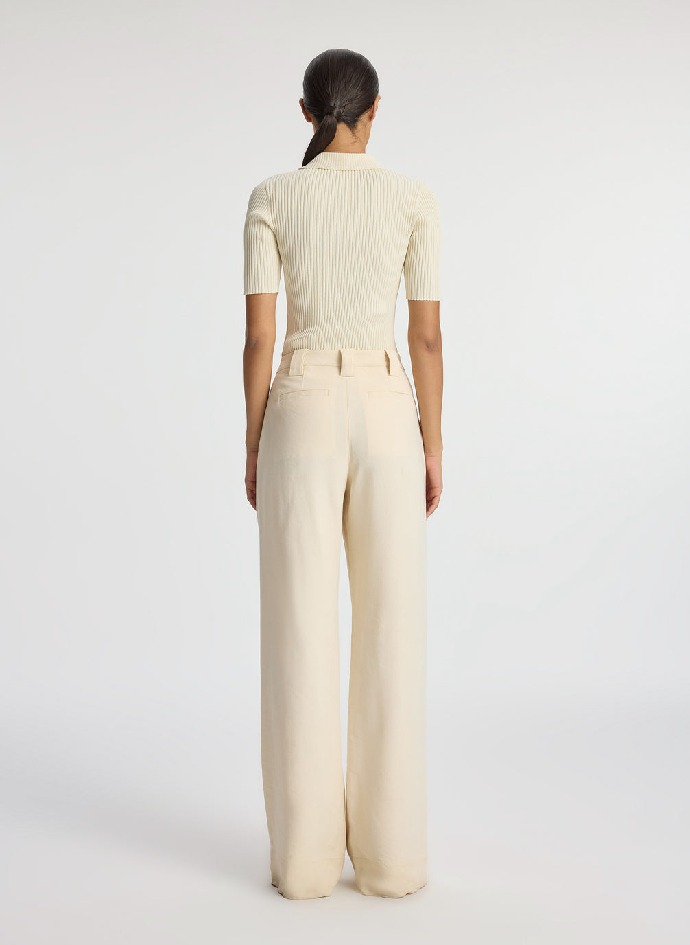 back view of woman wearing cream short sleeve collared top and beige pants