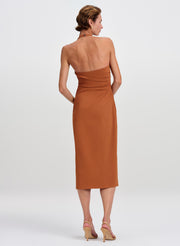 A woman shown from the back wearing a midi-length terracotta dress and nude high heels against a light gray studio background.