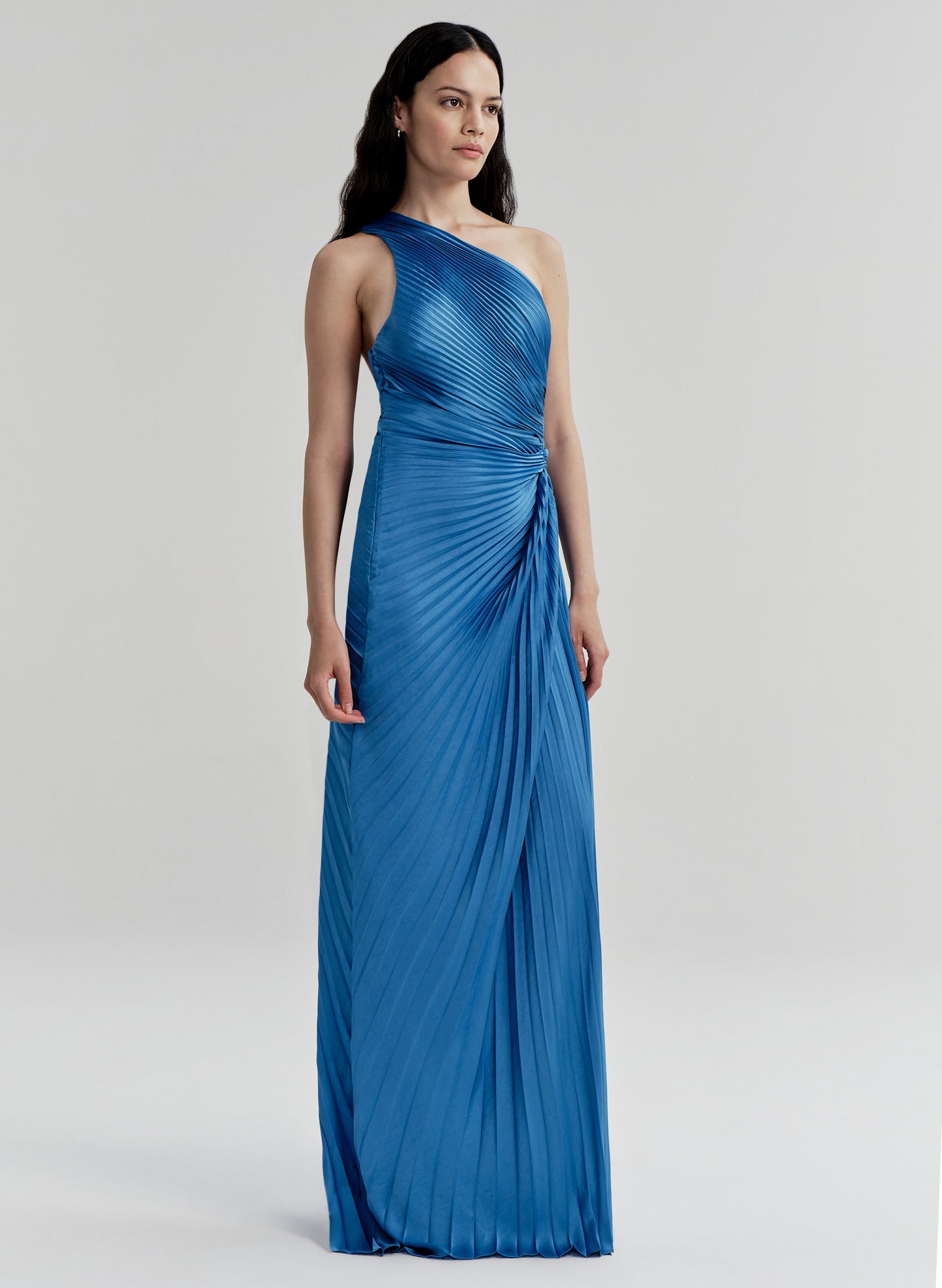Woman wearing a blue pleated one-shoulder gown against a white background