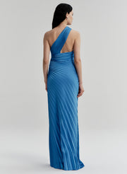 Woman wearing a blue pleated one-shoulder gown against a white background